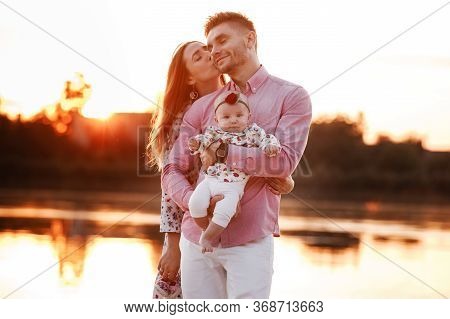 Happy Young Family Near Lake, Pond. Family Enjoying Life Together At Sunset. People Having Fun In Na