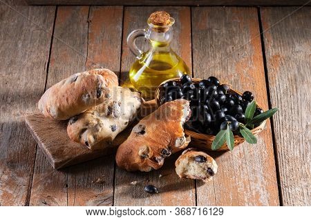 Traditional Italian Puccia Breads With Black Olives On A Cutten Board With Olive Oil And Fresh Black