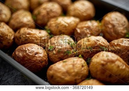 Close up with selective forus on homemade roasted whole potatoes in jackets. With butter, rosemary and thyme. Served in metallic dish placed on gray stone table.