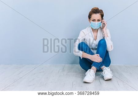 Girl With A Medical Mask Speaks On The Phone Sitting On The Floor. Concept On The Theme Of Coronavir