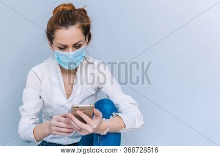 Girl With A Medical Mask Speaks On The Phone Sitting On The Floor. Concept On The Theme Of Coronavir