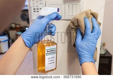 Person In Gloves Disinfecting Light Switch Panel Surface With Disinfectant Spray To Kill Germs, Bact