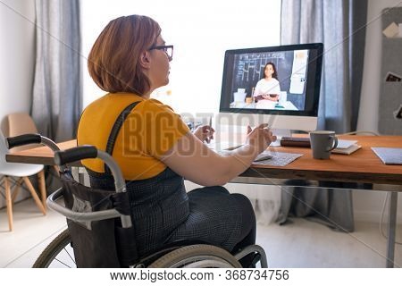 Young disabled tutor sitting in wheelchair and helping black student girl with hometask online while working remotely