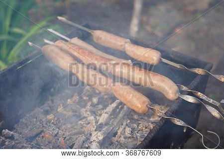 Close Up Of Toasted Sausages On Skewers. Succulent Kupaty Roasting On Chargrill. Concept Of Picnic O