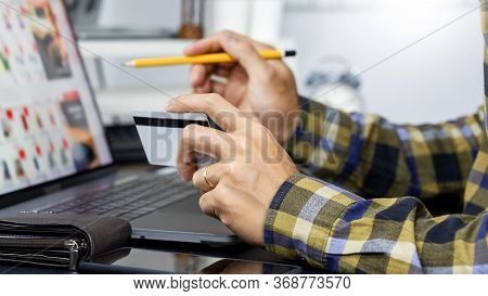 Asian Man Holding Credit Card To Online Shopping With Laptop Computer And Entering Security Code, In