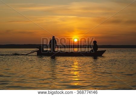The Fishermen And Boat Silhouette On The Lake.