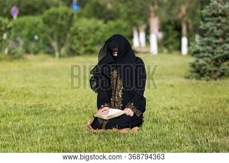 Islamic Woman Prayer In A City Park. Islamic Woman Performs Morning Prayer Sitting On Green Grass In