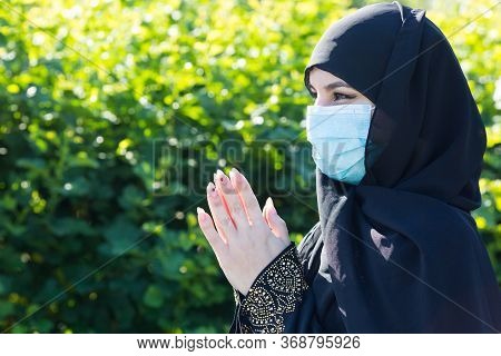 Islamic Woman In Protective Medical Mask Prays To God. Muslim Woman In A Medical Mask Prays On The S