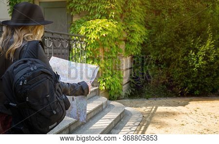 A Girl In A Leather Jacket, Hat , With A Backpack Examines A Map On A Journey.