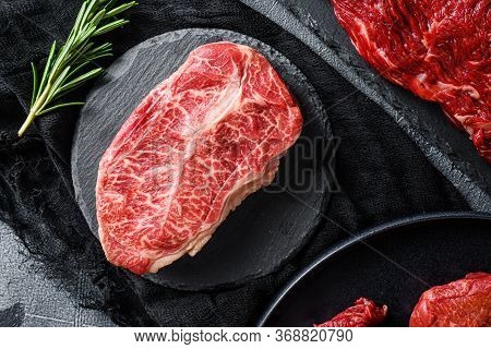 Raw Top Blade Cut Black Angus Organic Steak On A Black Plate And Stone Slate With Seasonings, Herbs 