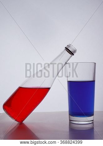 Composition From A Bottle And Glasses With Multicolored Liquid On A White Background. The Bottle Res