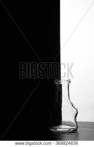 A Small Bottle On A Black And White Background. Half Black And Half White