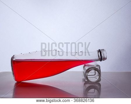 Glass Bottle With Red Liquid Inside Lies On A Small Bottle Of White Background