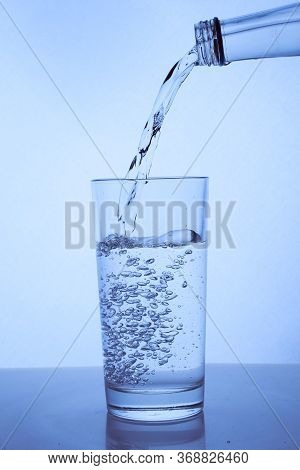 Fresh Clean Water Is Poured From A Bottle Into A Glass Cup. Light Background.