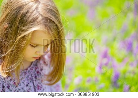 Small, Beautiful, Sad Girl Alone In A Field Of Purple Flowers. Child Is Unwell Because Of The Heat. 