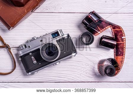 Vintage Film Rangefinder Camera With Leather Case And Photographic Film On White Wooden Table. The V