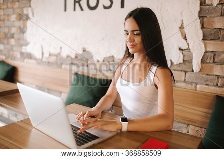 Attractive Girl Working On Laptop In Cafe. Beautiful Girl Using Computer For Work. Girl Drinking Cap