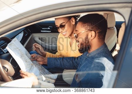 Car Trip. Happy Black Spouses Looking At Road Map Sitting In Car Traveling On Summer Vacation. Selec