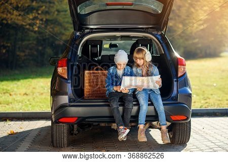 Agreeable Boy And Girl Are Looking At The Road Map While Sitting In The Autos Trunk And Discussing T