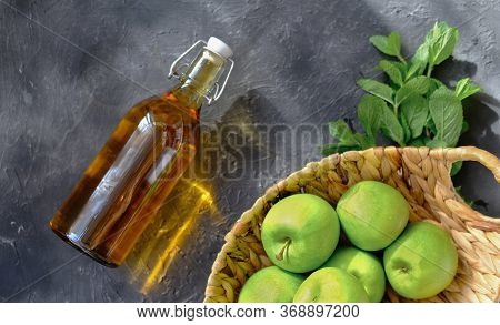 Apple Vinegar And Green Apples In A Basket. Bottle Of Homemade Apple Organic Vinegar Or Cider On Gre
