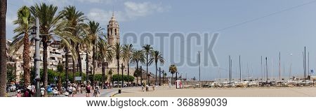 Barcelona, Spain - April 30, 2020: People On Urban Street With Palm Trees And Church Of Saint Bartol