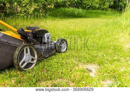Lawn Mower On Green Grass In Garden Near The Forest. Machine For Cutting Lawns. Summer Work On The F