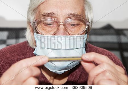 Elderly Woman In A Medical Mask. The Epidemic And Thermometer