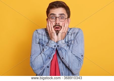 Portrait Of Emotional Shocked Scared Guy Opening Eyes And Mouth Widely, Putting Hands To Face, Havin