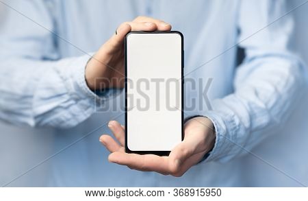 Man's Hand In A Blue Shirt Holding Smartphone With Blank Screen. Take Your Screen To Put On Advertis