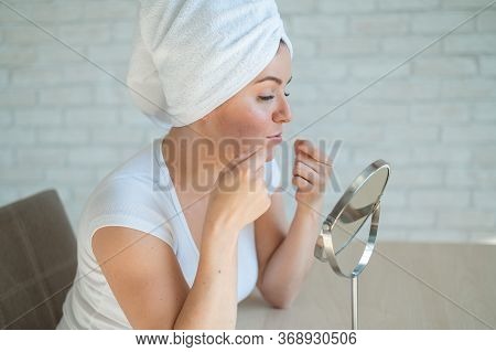 A Woman Looks In A Table Mirror And Crushes Acne On Her Chin. An Unhappy Girl With Problem Skin Does