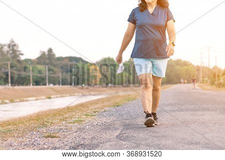Sportive Woman Take Off Protective Mask While Jogging For Easier Breathing On Road Beside Irrigation