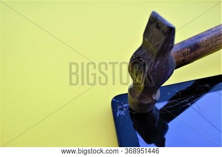 An Old Hammer With A Worn Wooden Handle Hits The Corner Of The Tablet Screen, The Glass Cracks, The 