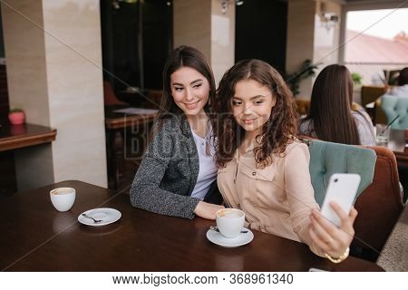 Attractive Young Women Making Selfie In Restairant. Women Drin Cappuccino On Terrace. Two Female Mak