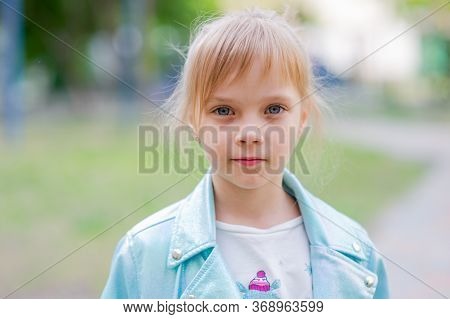 Close Up Portrait Of Young 6-7 Year Old Girl. Girl 7 Years Old Outdoors Portrait In A Blue Jacket. L
