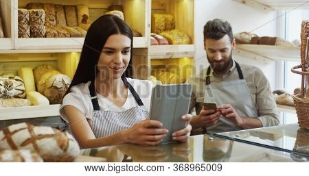 Caucasian Pretty Woman Seller Scrolling And Taping On The Tablet Computer While Standing At The Coun