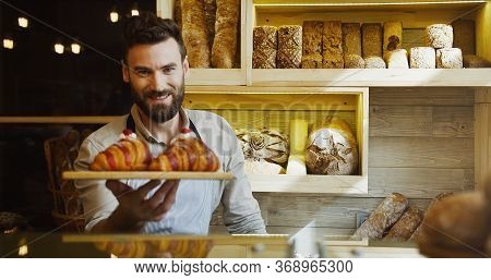 Portrait Of The Handsome Young Male Baker Smiling While Posing With Croissants On The Tray In The Sh