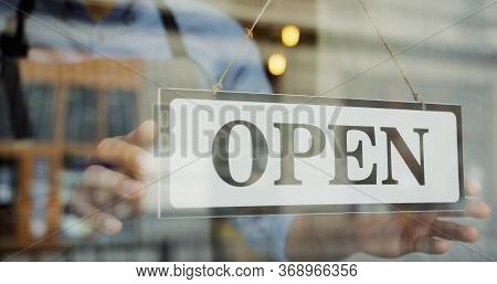 Close Up Of The Male Caucasian Hands Turning A Signboard On The Glass Door Of The Shop From Closed T