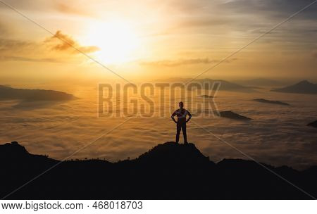 Silhouette Man Standing And Akimbo On Peak Of Stone Rock In Mountain And Watching To Sunrise Fog, Mi