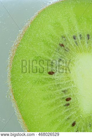 Close-up Of Kiwi Fruit In Liquid With Bubbles. Slice Of Green Ripe Kiwi Fruit In Sparkling Water. Ju