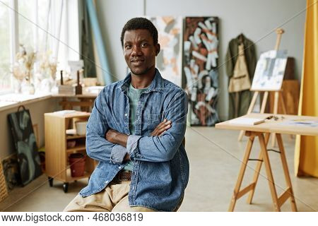 Young Confient Craftsman In Casualwear Sitting In Front Of Camera Against His Workplace, Easel With 