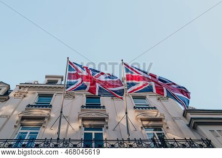 Low Angle View Of Two Union Jack British Flags Flowing In The Wind, On Poles Outside A Building In L