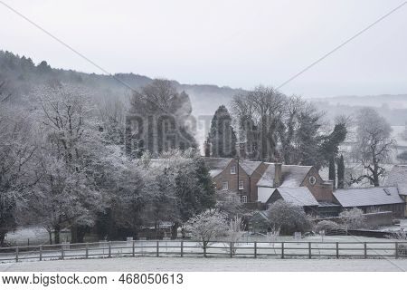 Beautiful Wintry Landscape Of Farm In Fog In English Countryside At Dawn With Hoarfrost Covering Tre