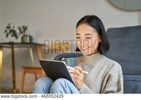 Smiling Korean Woman Sitting With Tablet And Pen, Drawing And Scatching Her New Project Or Design, W
