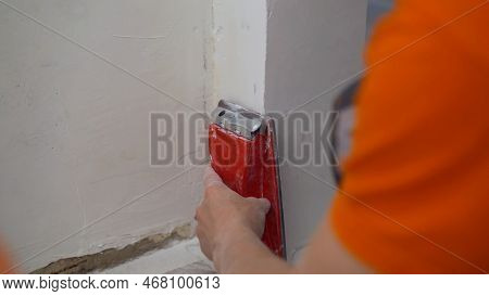 The Builder Grinds The Wall From Irregularities After Applying Putty. Sanding And Leveling The Wall 