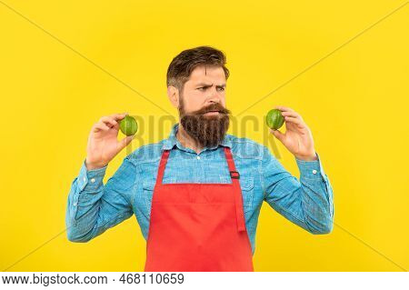 Worried Man In Red Apron Looking At Fresh Limes Citrus Fruits Yellow Background, Fruiterer