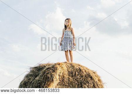Pretty Little Girl Stand At Top Of Haystack Looking Away. Full Length Photo, From Below View. Restin