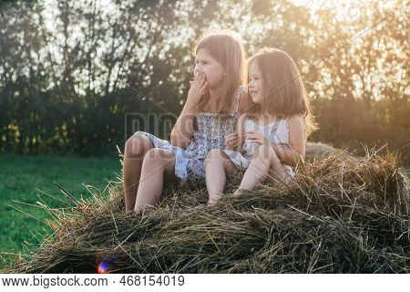 Pretty Little Girls Sitting Together At Top Of Haystack On Sunny Day. Carefree Children Resting On H