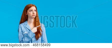 Envy And Sad Sulking Moody Redhead Teenage Girl In Nightwear, Looking And Pointing Upper Left Corner