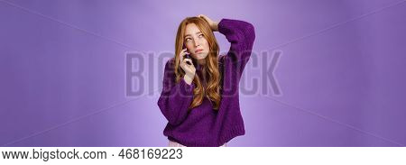 Confused Cute Redhead Female Making Appoinment Via Mobile Phone Scratching Back Of Head And Squintin