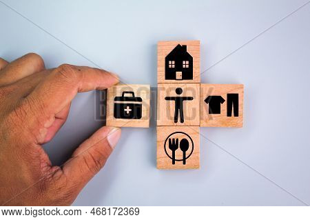 Wooden Cube With Icons Of Food, Clothing, Housing, Medical Bag, Four Basic Human Needs Concepts. The